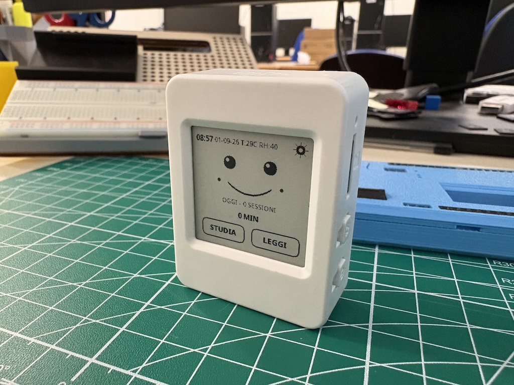 Piccolo dispositivo OpenStudy Desktop Companion con display e-paper acceso accanto a un libro e a un quaderno.